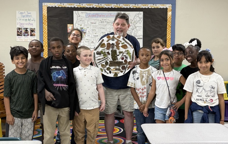 an adult surrounded by students holding a nature mandala