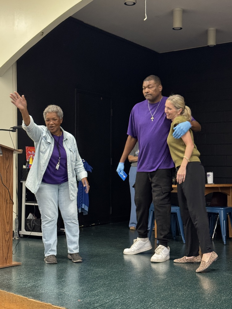 three people on a stage, two receiving giftcards from the other