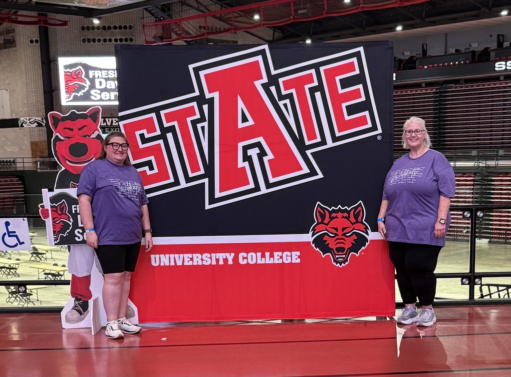 Two El Dorado School District educators stand beside a large Arkansas State University sign inside First National Bank Arena during the Special Olympics Arkansas RecFest.