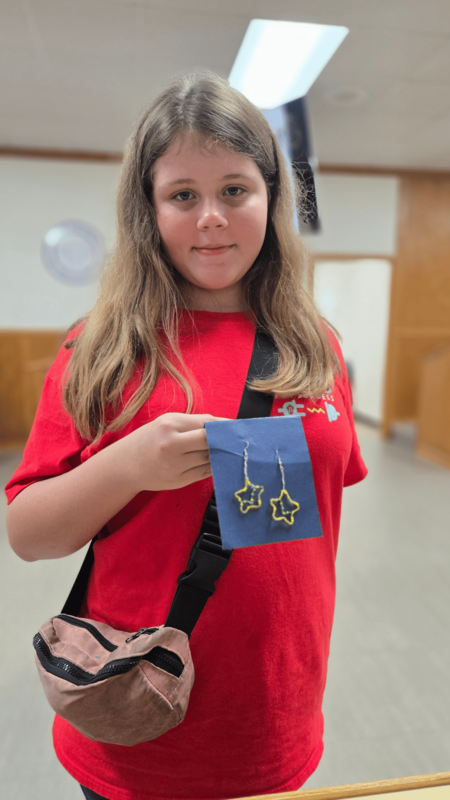 6. Elementary Beta Club student wearing a red shirt and displaying a pair of handmade star-shaped earrings entered in the National Beta Convention.