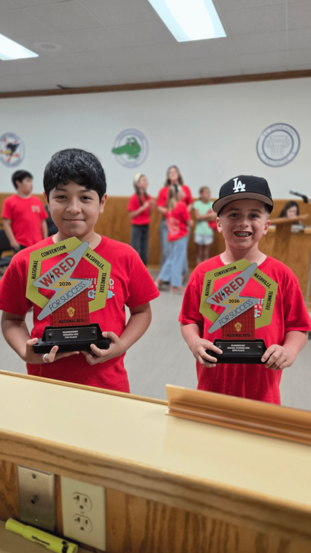 5. Two elementary students wearing red Beta Club shirts and holding National Beta Convention awards for seventh place in Spanish and tenth place in social studies.