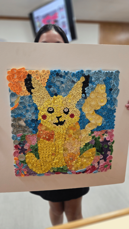 . Close-up of a detailed paper-quilling artwork depicting Pikachu, created with tightly rolled strips of colorful paper.