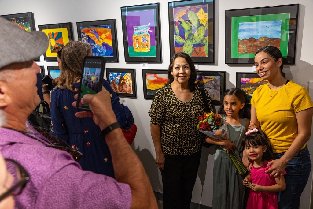 Photo of someone taking a picture of a family posing in front of daughter's artwork