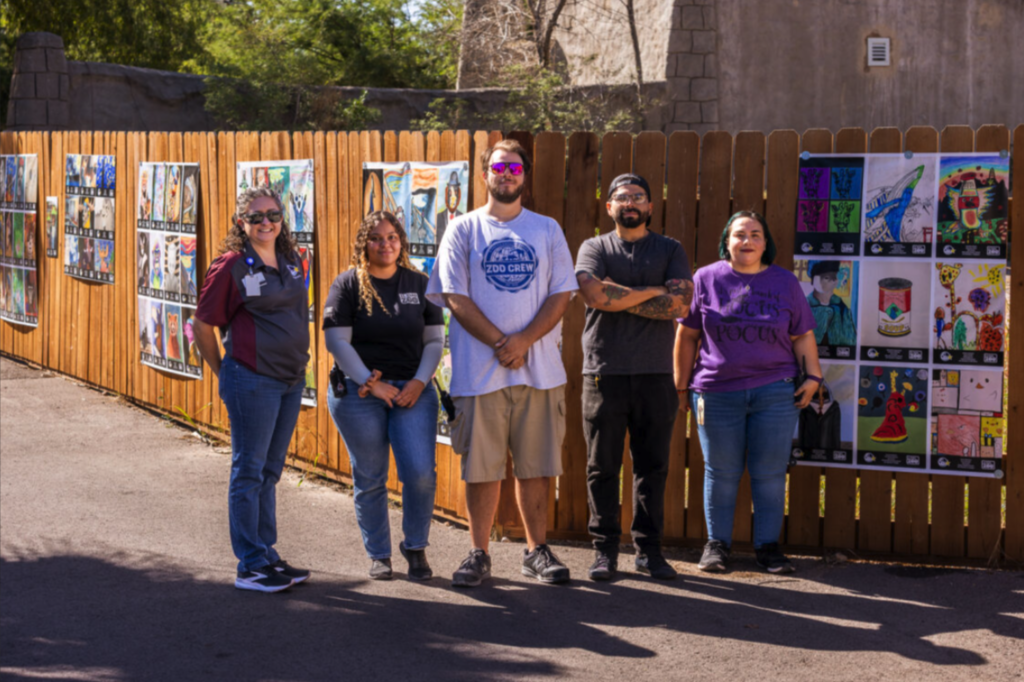 El Paso ISD and El Paso Zoo staff smile for a photo in front of the Furry & Feathered Art History Exhibit at the zoo
