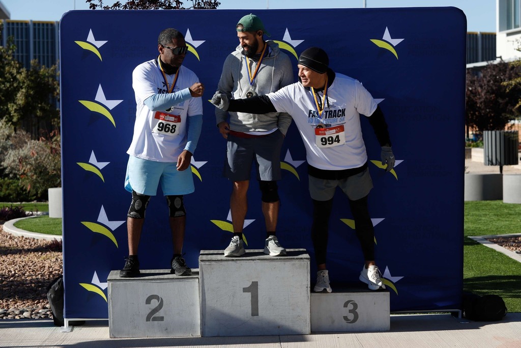 Top three runners for the Fast Track to the Future 5K take photos on podium and fist bump each other
