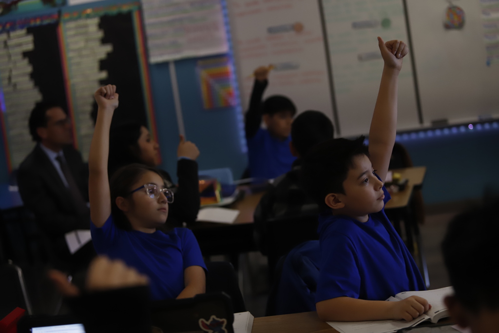 Students at Murphree PK-8 raise their hands during class