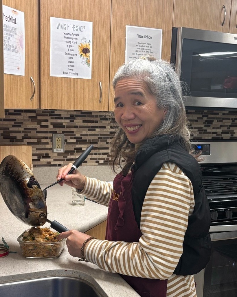 Photo of Healthy Living cooking class. Participate smiles while transferring food in pan to a bowl