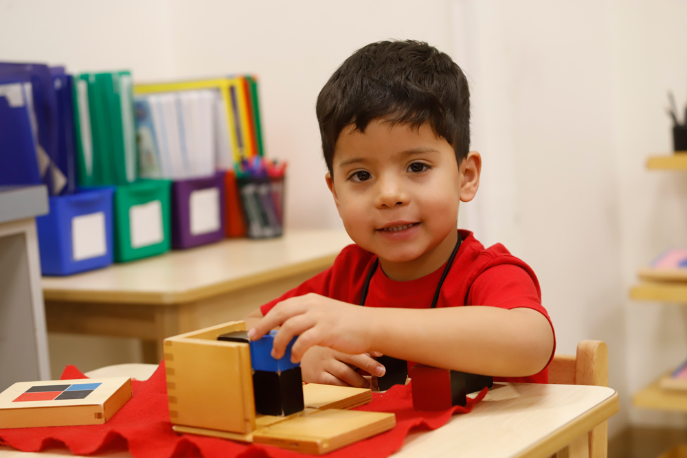 Montessori student smiles at camera while working