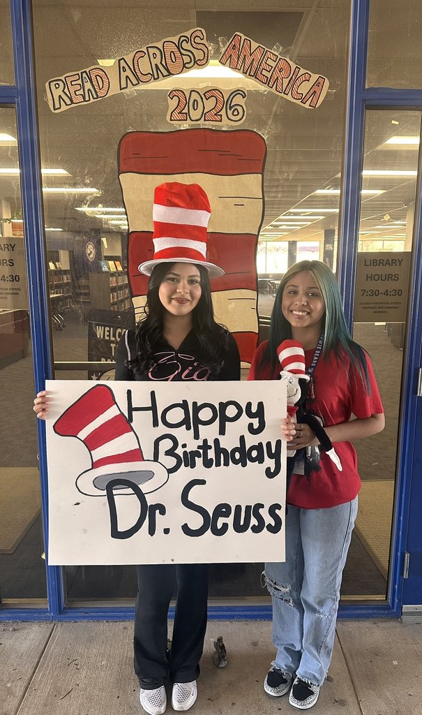 Two Bowie High School students smile for a photo while holding a sign that says Happy Birthday Dr. Seuss