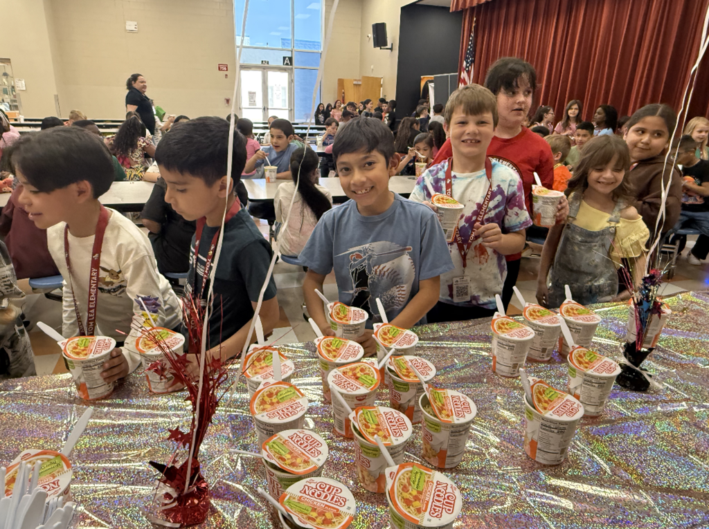 Students smile for a photo while receiving their ramen noodles cup