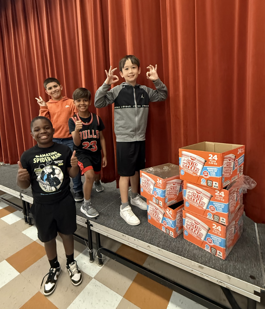 Four students smile next to a few empty boxes of ramen noodles
