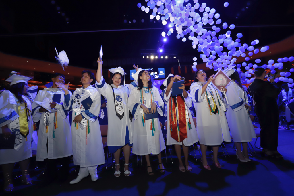 Photo of Bowie High School graduates smiling and throwing caps after graduation while balloons falling in the background