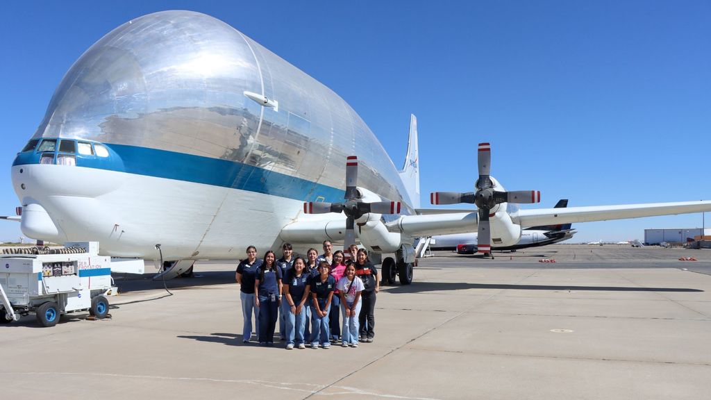 A group of Young Women's Academy students take photo in front of large plane