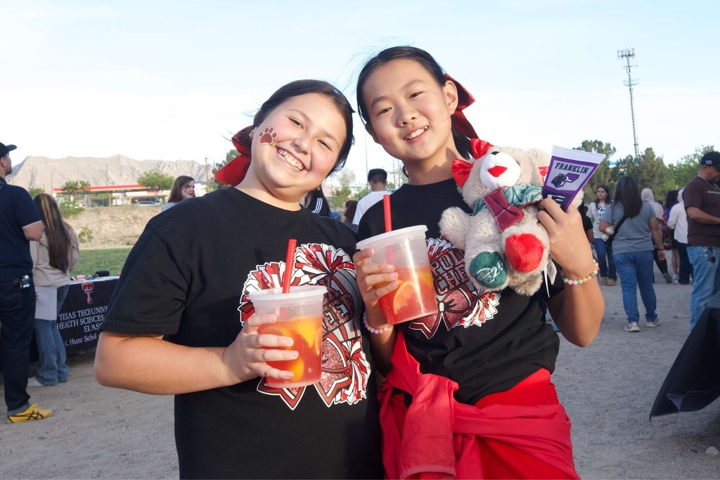 Two students smile for a photo holding drinks , teddy bear, and mini Franklin flag
