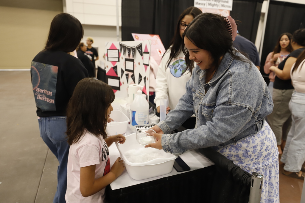 High School students gives young child a bowl to prepare for science experiment