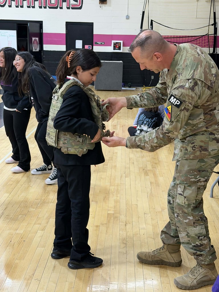Young Women's Academy student tries on army vest while community member helps her 