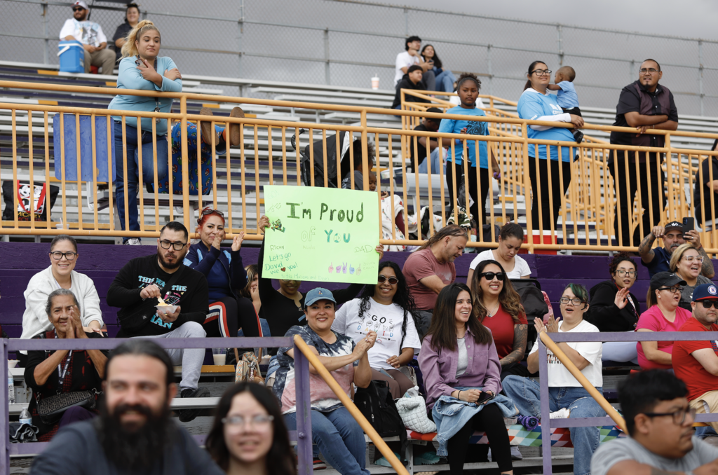 Parents cheer on students during Unidos Game Parade holding sign