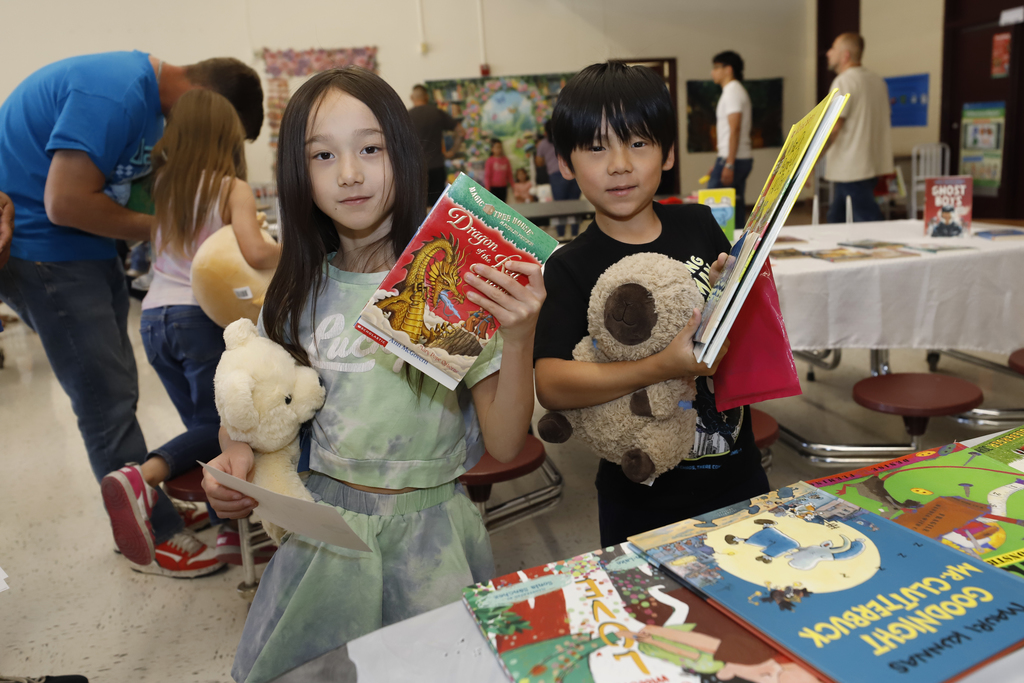 Two students smile while holding books and stuff animals