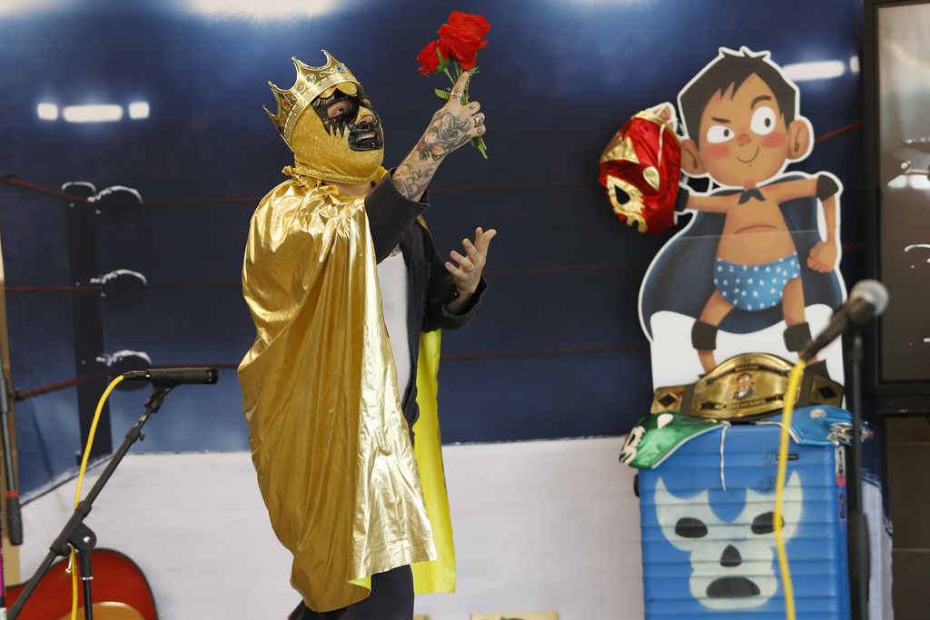 Author gives storytelling presentation while dressed as a luchador with a gold crown while holding up a rose