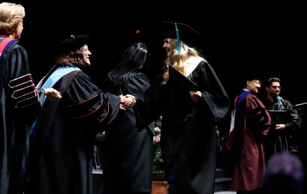 Austin High School P-TECH program graduate shakes hands with EPCC staff after receiving diploma