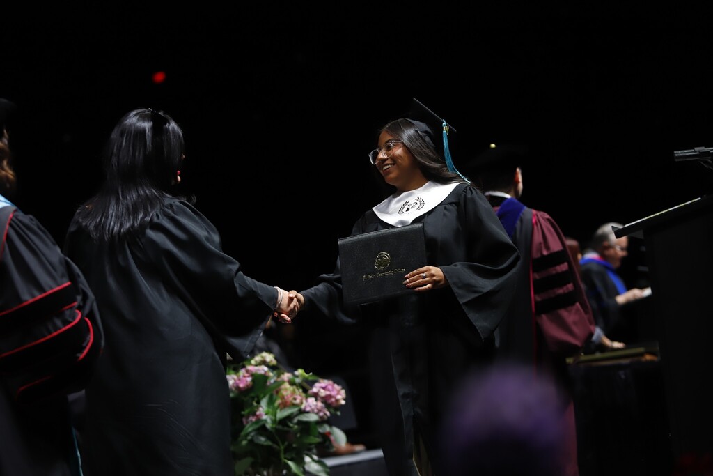 Austin High School P-TECH program graduate shakes hands with EPCC staff after receiving diploma