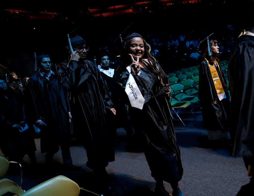 Transmountain Early College High Schoo graduate smiles with a peace sign while walking into graduation ceremony