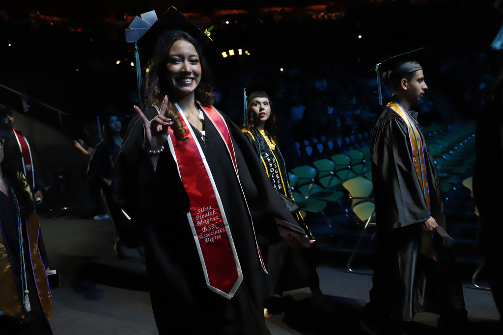 Silva Health Magnet student smiles with foxes hand symbol while walking into the EPCC graduation ceremony