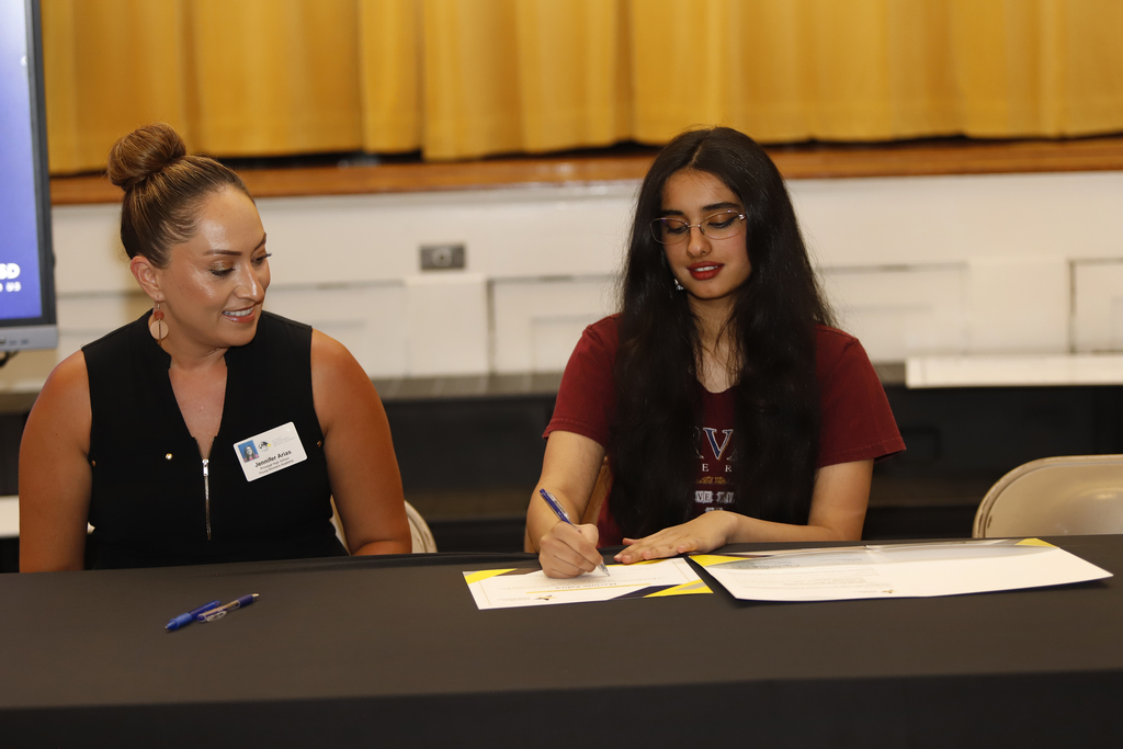 Young Women's Academy student signs paper next to her principal during El Paso ISD Education Foundation scholarship ceremony