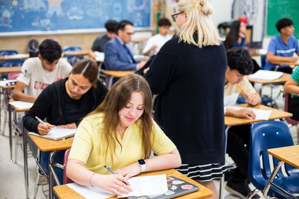 Students writing in class as teacher passes by
