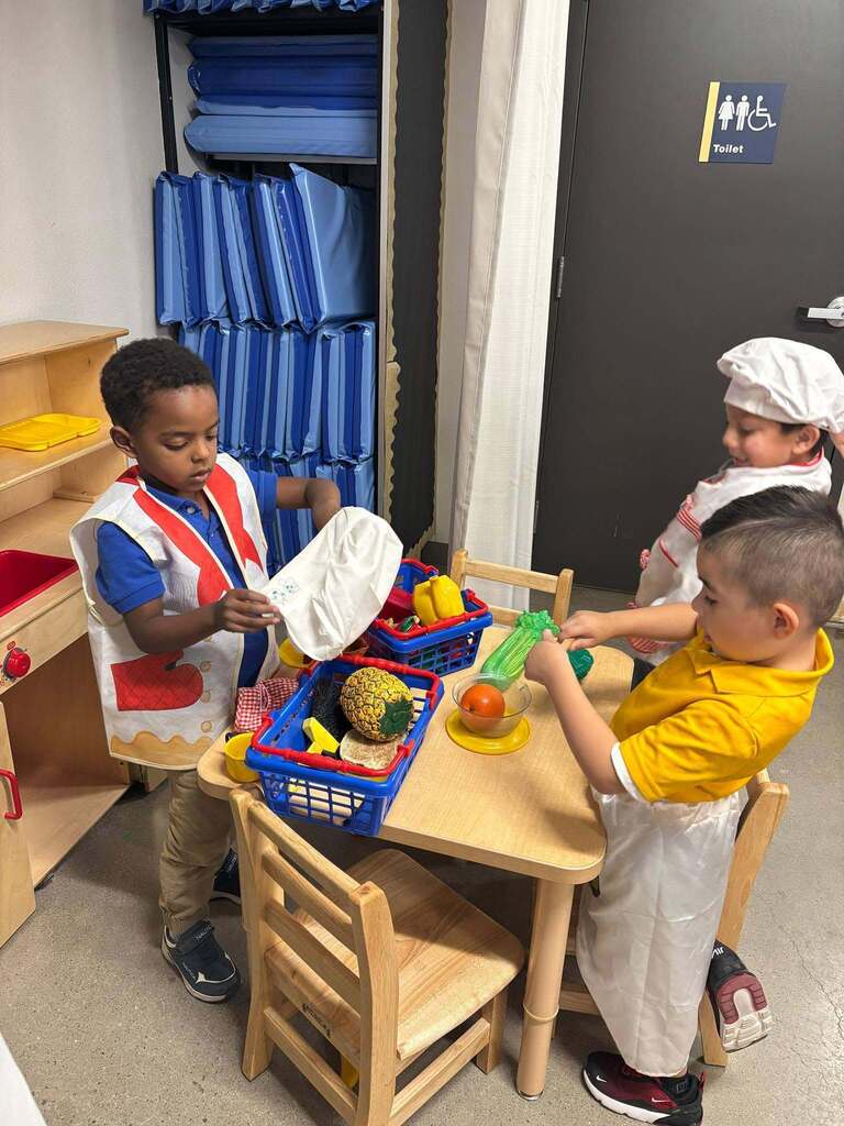 Elementary Murphree students in class working with fake fruits and veggies while wearing chef attire