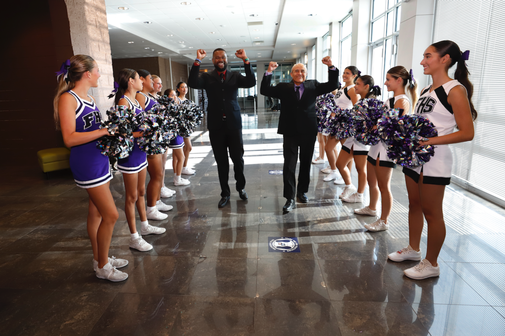 Ramon Rosales Jr. of Lundy Elementary School and John Matthews of Jefferson Silva High School walk down hallway cheering with hands up as Franklin cheerleaders cheer them on