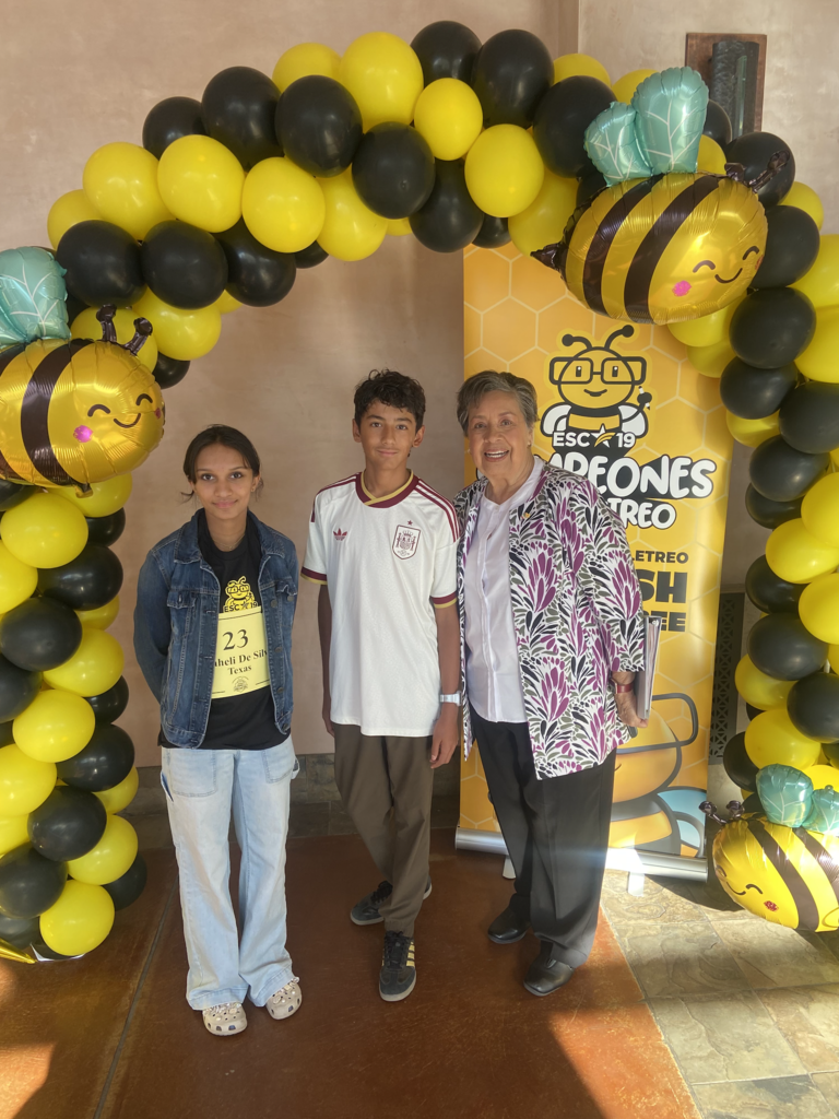 Photo of Ferrán Martínez Caloca from Wiggs Middle School and Shaheli De Silva from Young Women's STEAM Research and Preparatory Academy smiling for a photo together at the National Spanish Spelling Bee with a judge