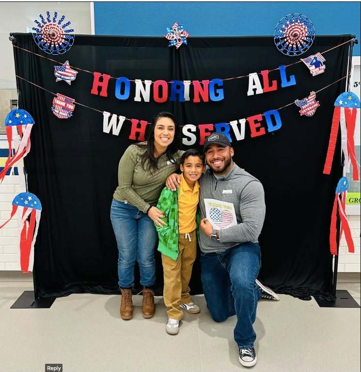 Parents and Murphree PK-8 student smile for a photo at military celebration at the campus with sign in background that says honoring all who served