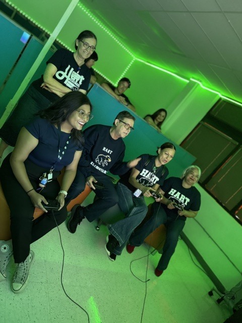 A group of people dressed in matching shirts are playing a video game in a green-lit room.