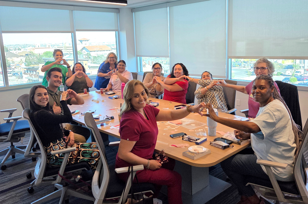 El Paso ISD employees smile for a photo holding up hand hearts during book club session