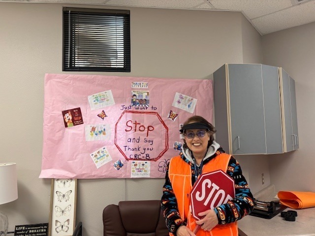 Volunteer smiles for a photo in front of thank you sign before heading out to crossing guard duty