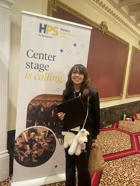 Vivian Lopez smiles with choir book in front of poster