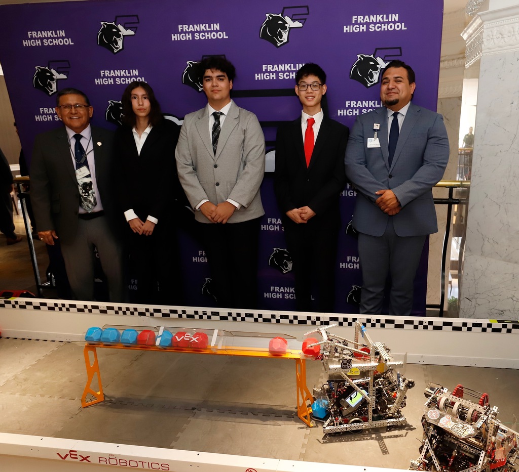 Franklin High School robotics team smiles for a photo in front of their robotics display