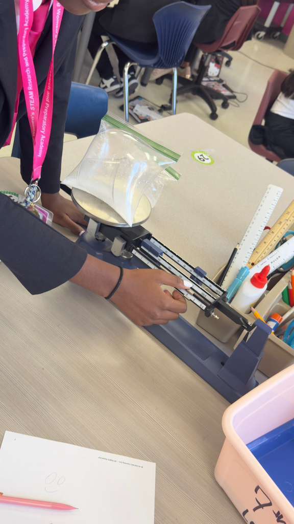Person in a classroom weighing an object in a plastic bag using a balance scale.