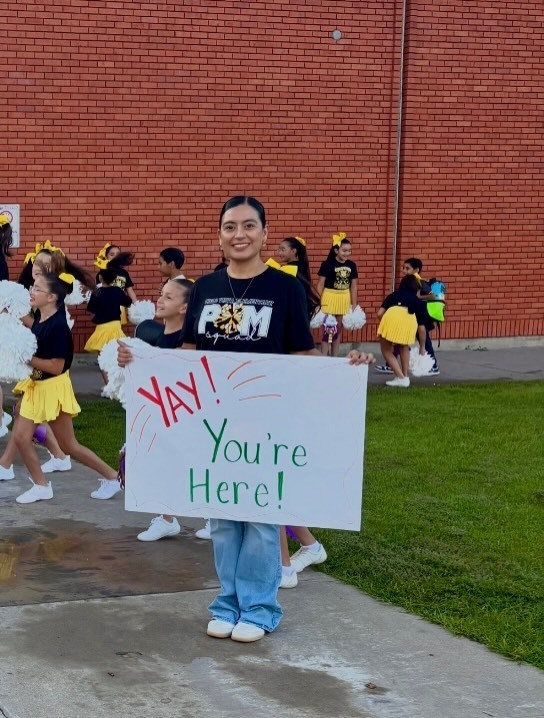 Cielo Vista Elementary School staff member welcomes students into school with signs that say "Yay! You're Here!"