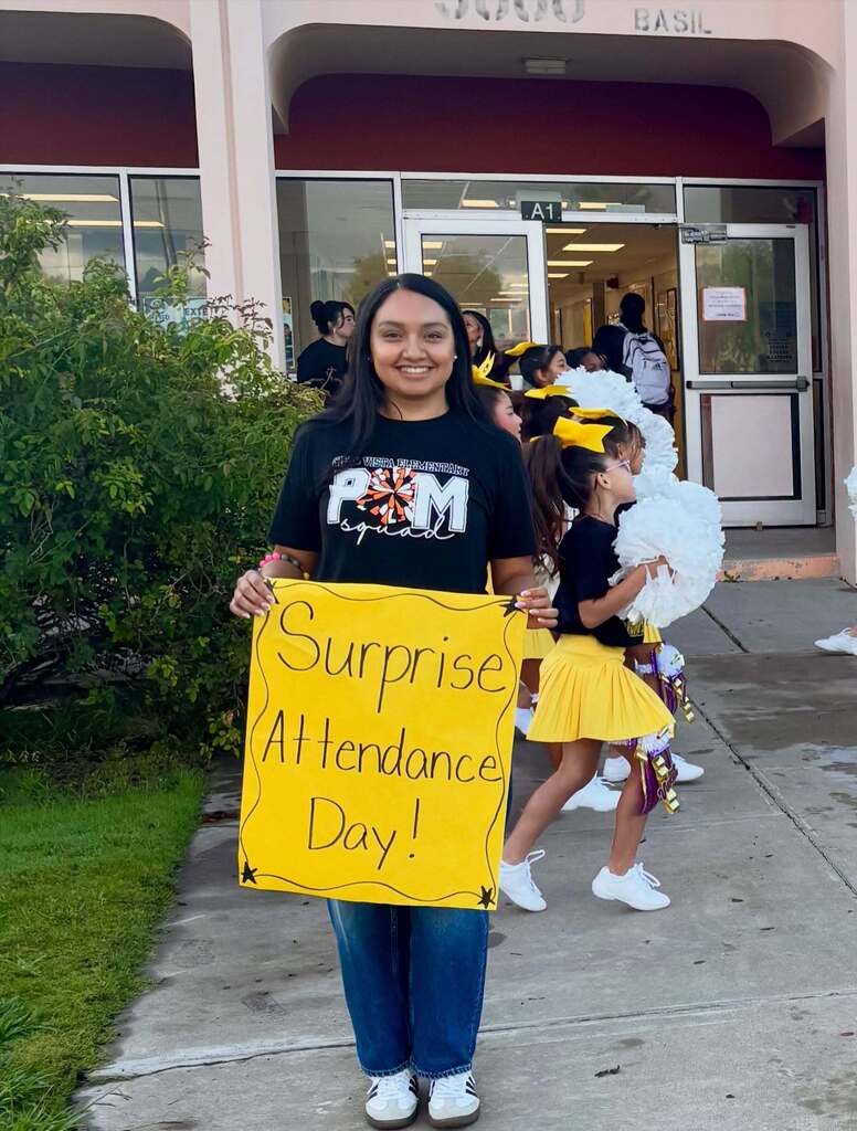 Cielo Vista Elementary School staff member welcomes students into school with signs that say "Surprise Attendance Day!"
