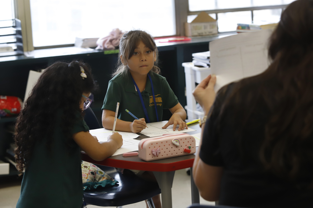 Student takes notes as teacher shows her a paper