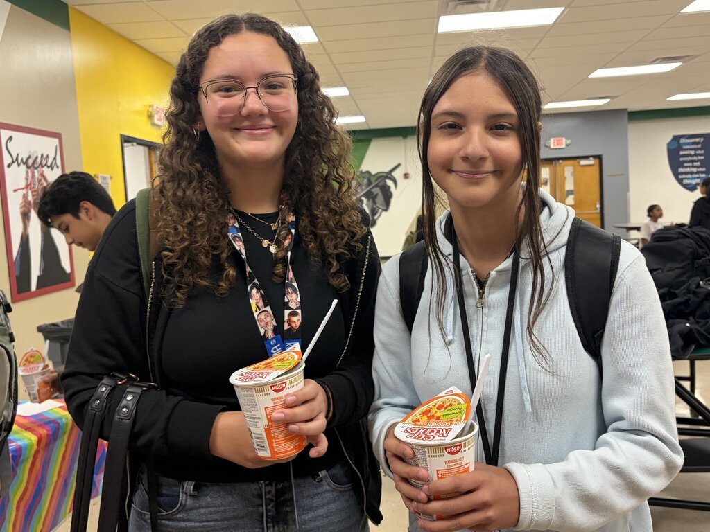 Two students smile with their cup of noodles