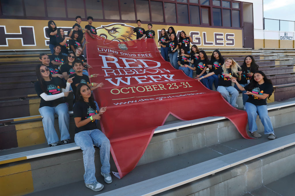 Andress High School students smile for a photo with giant red banner that says Living Drug Free Red Ribbon Week October 23-31 www.dea.gov/redribbon