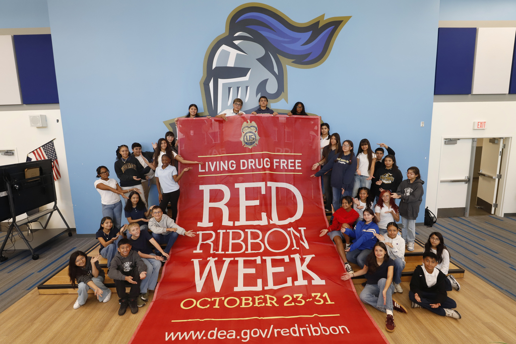 Navarrete Middle School students smile for a photo with giant red banner that says Living Drug Free Red Ribbon Week October 23-31 www.dea.gov/redribbon