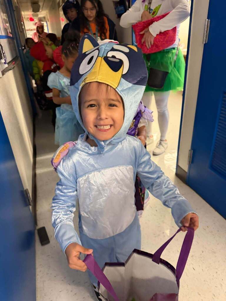 Student smiles for a photo in Bluey costume holding out bag for candy