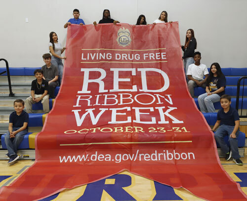 Kids in a gym hold up a Red Ribbon Week banner