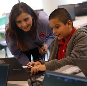 A teacher sits with a student and looks at a computer