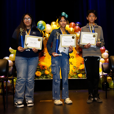 Three students stand on stage at the spelling bee