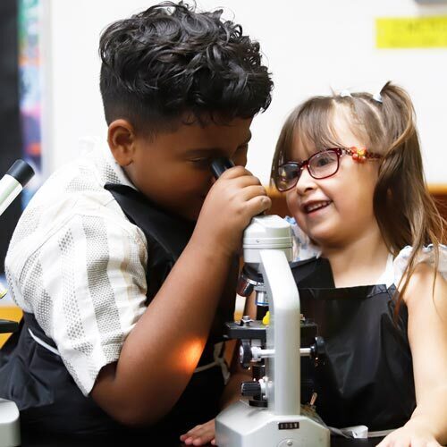 Students in a classroom use a microscope